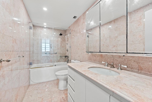 full bathroom with tasteful backsplash, bath / shower combo with glass door, toilet, vanity, and tile walls