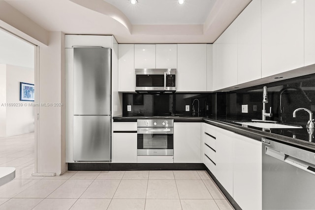 kitchen with sink, stainless steel appliances, light tile patterned floors, tasteful backsplash, and white cabinets