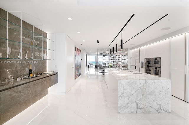 kitchen featuring a spacious island, decorative light fixtures, light stone counters, and sink