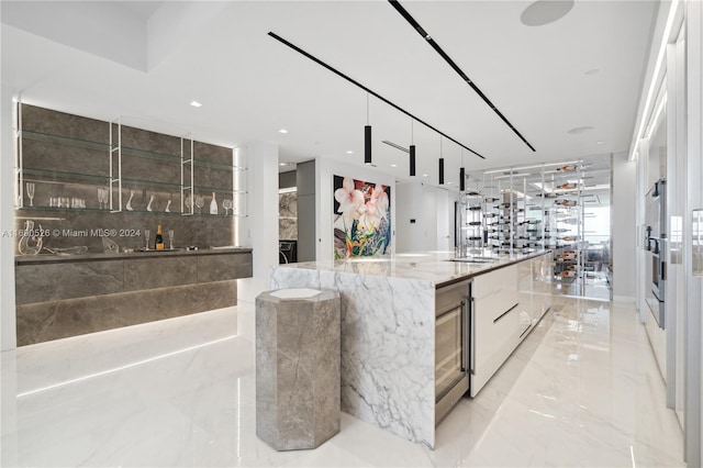 kitchen with a large island, beverage cooler, light stone counters, a fireplace, and white cabinets