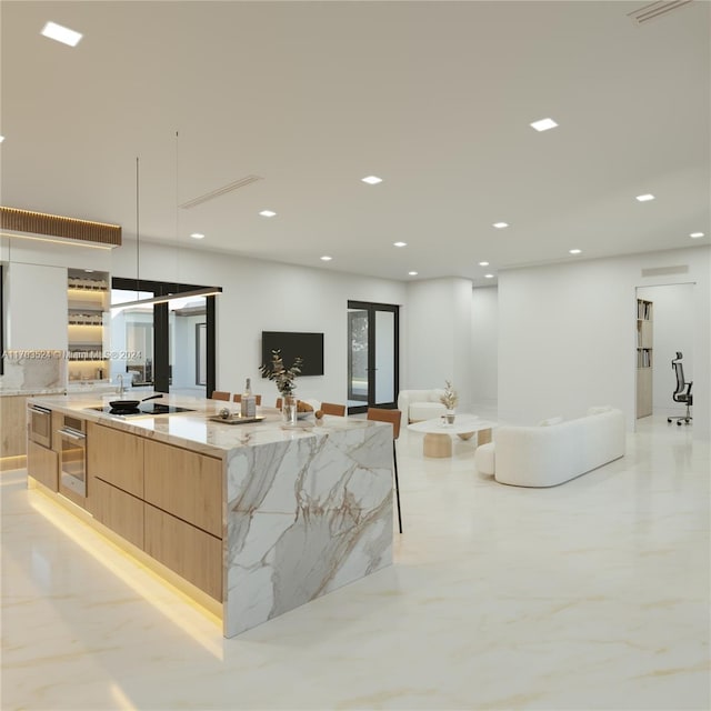 kitchen with stainless steel oven, a large island with sink, black stovetop, light brown cabinetry, and light stone counters