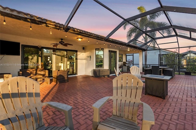 patio terrace at dusk with glass enclosure, ceiling fan, and a fire pit