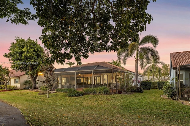 back house at dusk with a lawn and glass enclosure