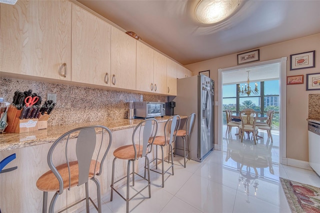 kitchen with light tile patterned floors, light stone countertops, light brown cabinetry, stainless steel fridge with ice dispenser, and a chandelier