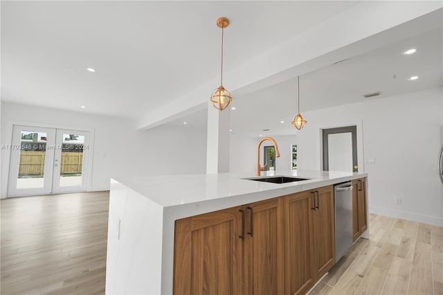 kitchen featuring dishwasher, sink, pendant lighting, a kitchen island with sink, and light wood-type flooring