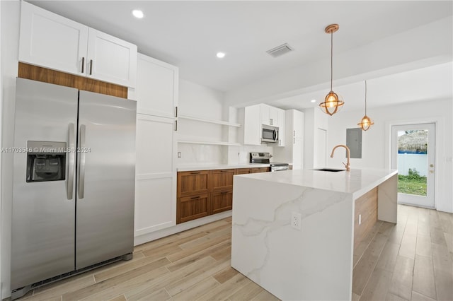 kitchen featuring appliances with stainless steel finishes, light stone counters, a kitchen island with sink, light hardwood / wood-style flooring, and white cabinetry