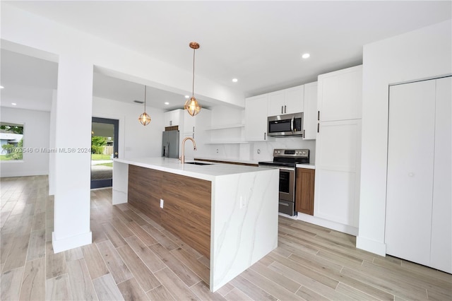 kitchen with light wood-type flooring, stainless steel appliances, sink, white cabinets, and an island with sink