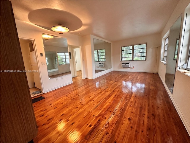 unfurnished living room featuring wood-type flooring, a wealth of natural light, and an AC wall unit