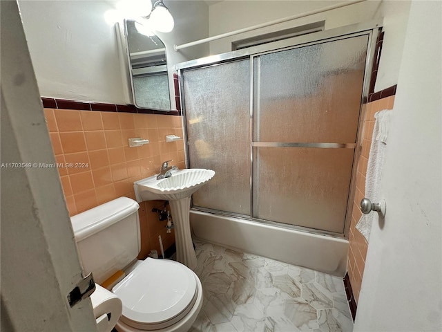 bathroom with shower / bath combination with glass door, toilet, and tile walls