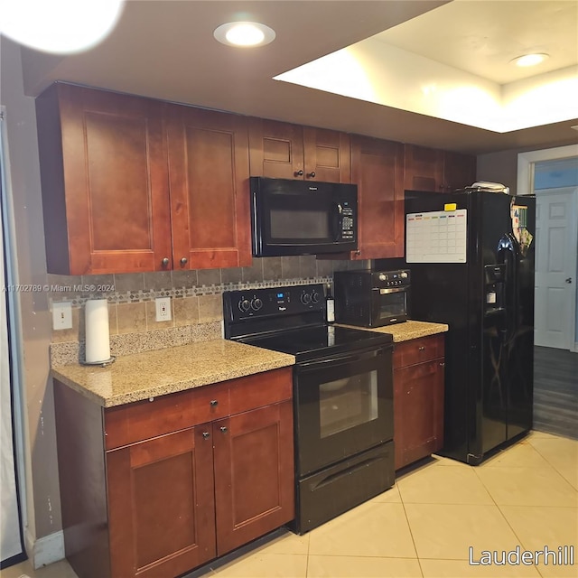 kitchen featuring light stone countertops, a tray ceiling, decorative backsplash, light tile patterned floors, and black appliances