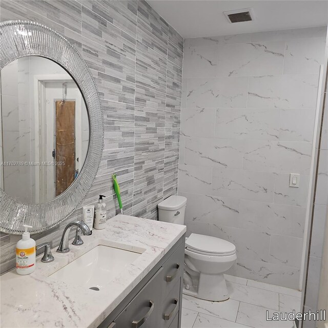 bathroom featuring vanity, tile walls, and toilet