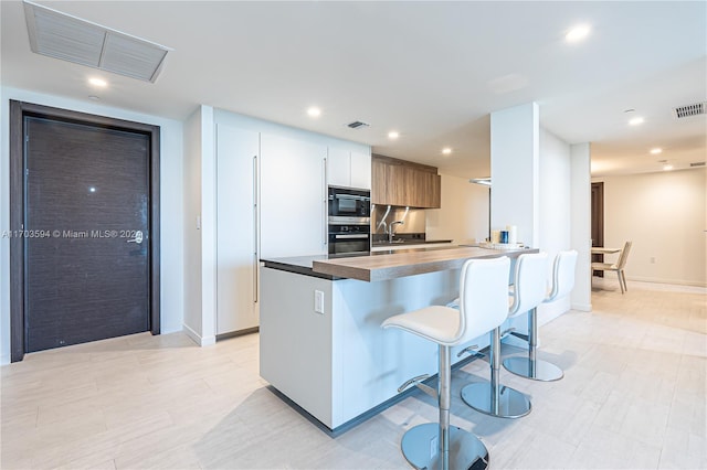 kitchen featuring a breakfast bar, sink, kitchen peninsula, appliances with stainless steel finishes, and white cabinetry