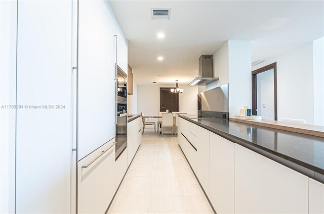 kitchen with white refrigerator, white cabinetry, wall chimney exhaust hood, and a notable chandelier