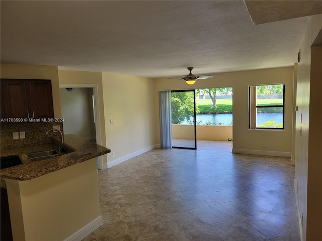 kitchen with decorative backsplash, kitchen peninsula, ceiling fan, sink, and a water view