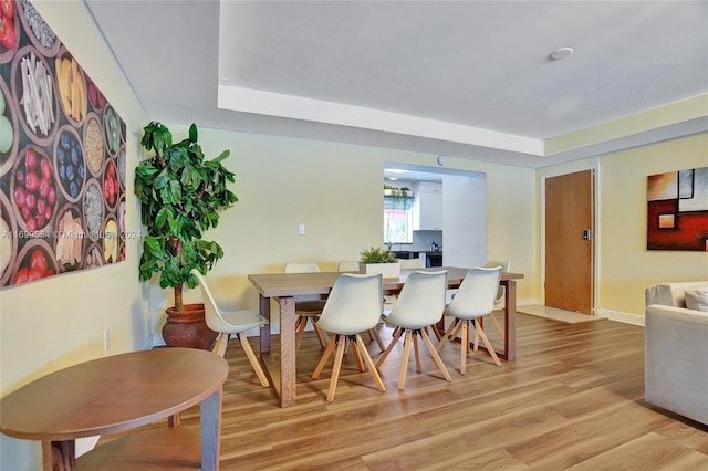 dining area with a raised ceiling and light hardwood / wood-style flooring