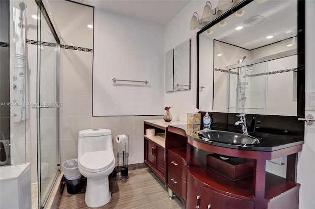 bathroom with vanity, toilet, a shower with shower door, and tile walls