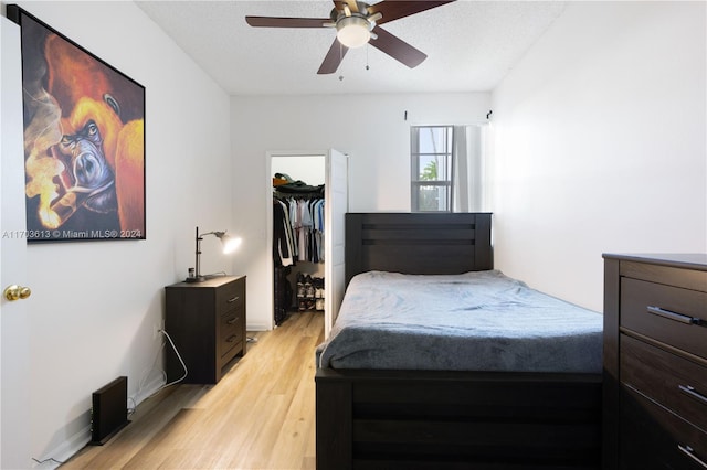 bedroom featuring a walk in closet, light wood-type flooring, a textured ceiling, ceiling fan, and a closet