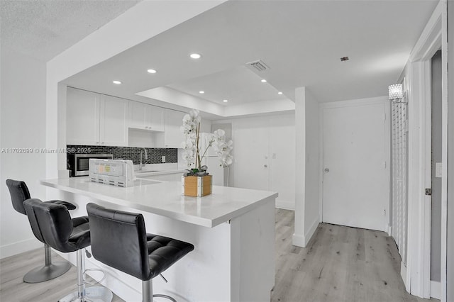 kitchen with white cabinetry, light wood-type flooring, kitchen peninsula, and a breakfast bar