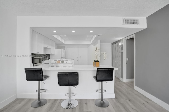 kitchen featuring a tray ceiling, a kitchen breakfast bar, kitchen peninsula, white fridge, and white cabinets