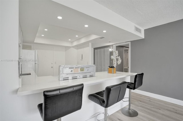 kitchen with a breakfast bar, white cabinetry, a tray ceiling, kitchen peninsula, and light wood-type flooring