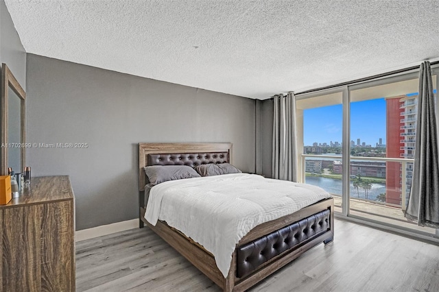 bedroom with access to exterior, light hardwood / wood-style floors, floor to ceiling windows, a water view, and a textured ceiling