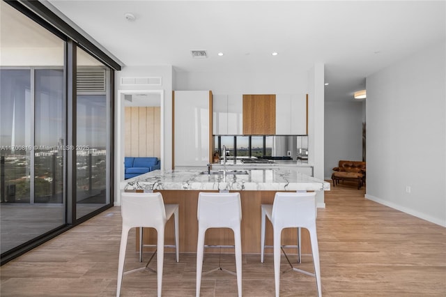 kitchen with a kitchen island with sink, white cabinetry, light stone counters, and a kitchen breakfast bar