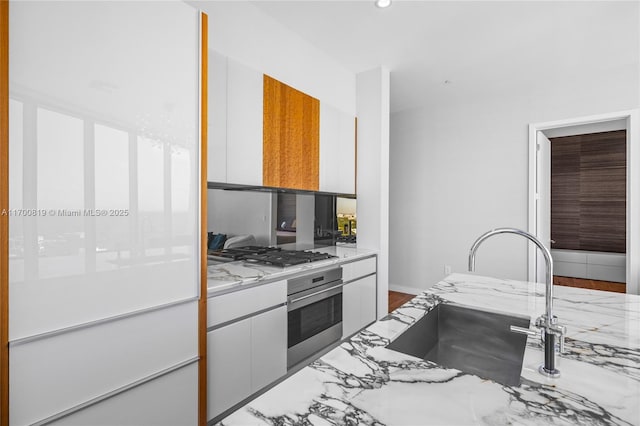 kitchen with white cabinets, sink, light stone counters, wood-type flooring, and stainless steel appliances