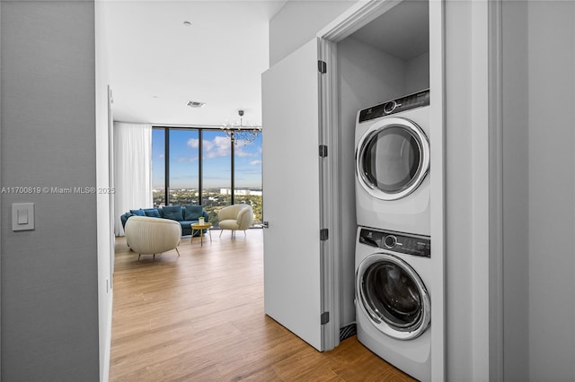 clothes washing area with stacked washer / drying machine, a chandelier, and light hardwood / wood-style flooring