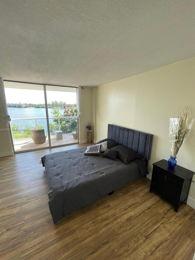 bedroom with access to exterior, floor to ceiling windows, a textured ceiling, and hardwood / wood-style flooring