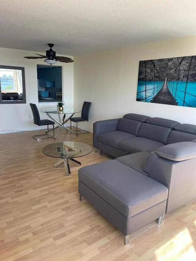 living room with ceiling fan, light hardwood / wood-style floors, and a textured ceiling