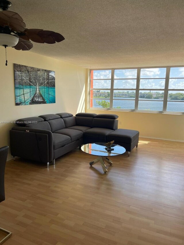 living room featuring a water view, a healthy amount of sunlight, a textured ceiling, and light wood-type flooring