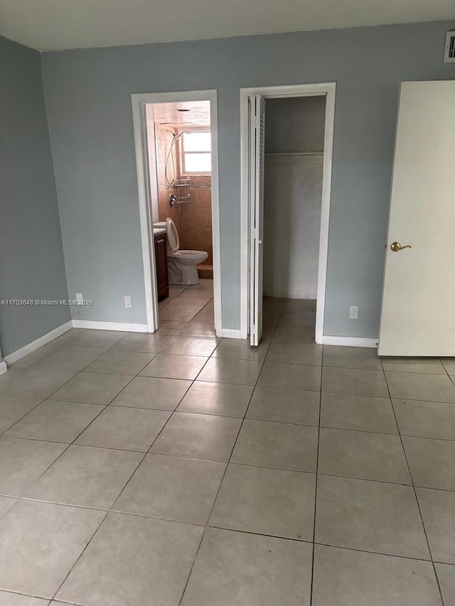 unfurnished bedroom featuring ensuite bathroom, a spacious closet, light tile patterned floors, and a closet