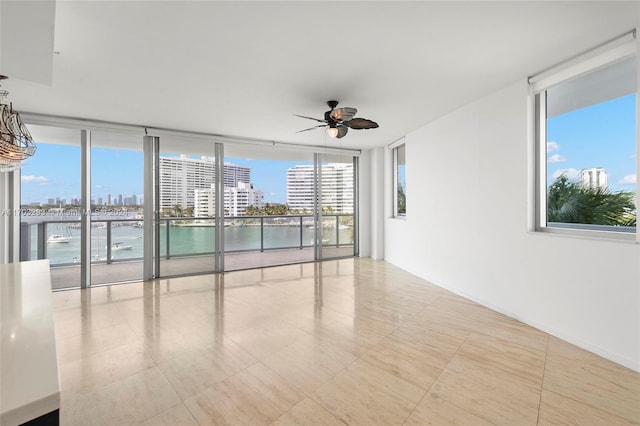 unfurnished room with floor to ceiling windows, ceiling fan, plenty of natural light, and a water view