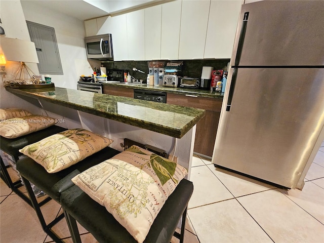 kitchen featuring decorative backsplash, a kitchen breakfast bar, dark stone counters, stainless steel appliances, and white cabinetry