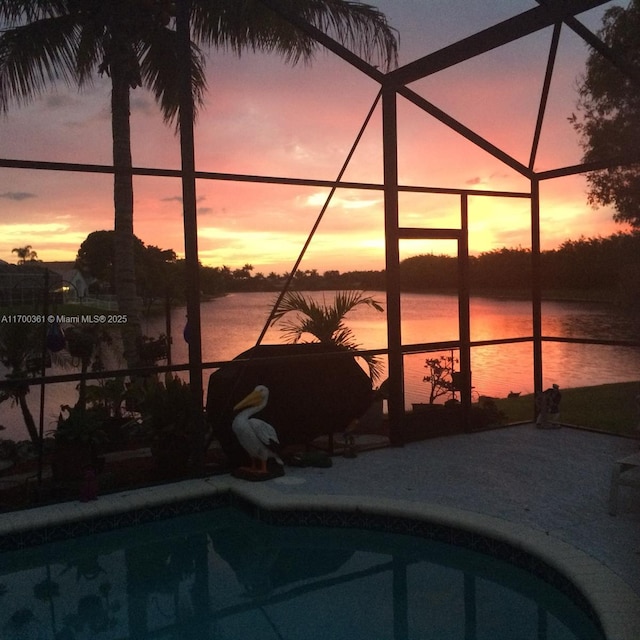 pool at dusk with a lanai, a patio, and a water view