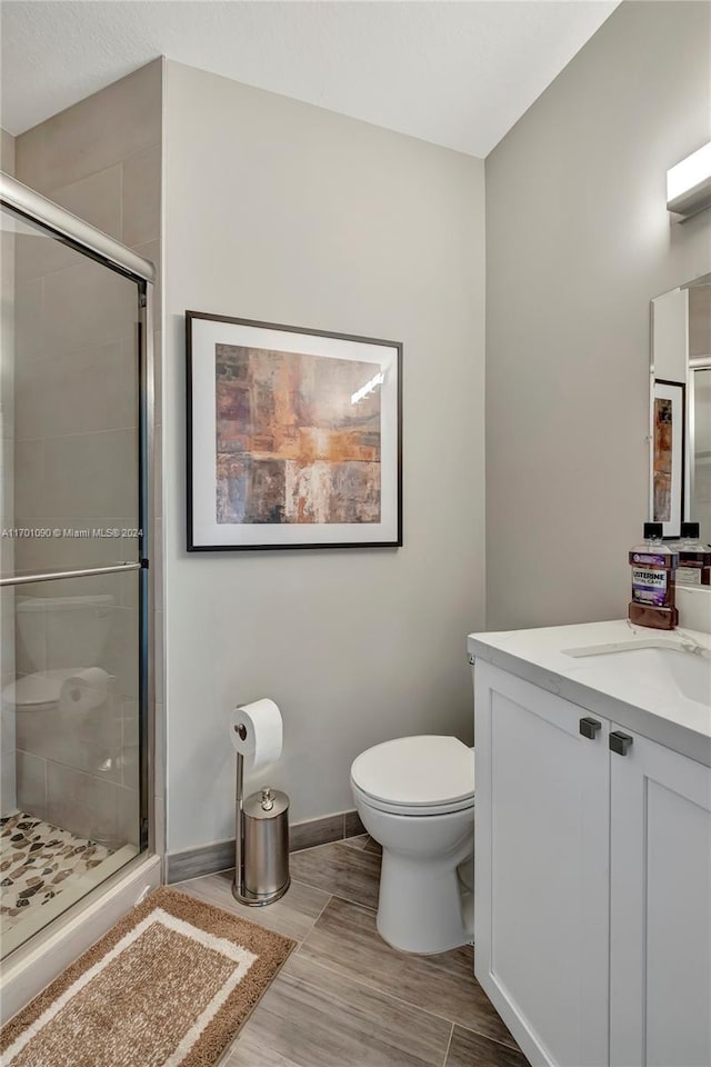 bathroom with hardwood / wood-style floors, vanity, toilet, and a shower with shower door