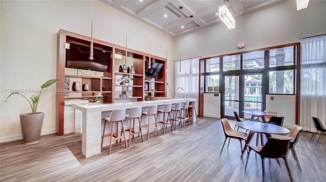 bar with french doors, a high ceiling, coffered ceiling, beamed ceiling, and light hardwood / wood-style floors