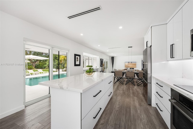 kitchen featuring light stone countertops, dark hardwood / wood-style flooring, stainless steel appliances, white cabinets, and a center island