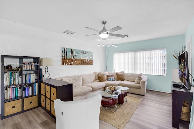 living room featuring light wood-type flooring, ceiling fan, and brick wall