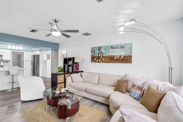 living room featuring hardwood / wood-style floors, ceiling fan, and brick wall