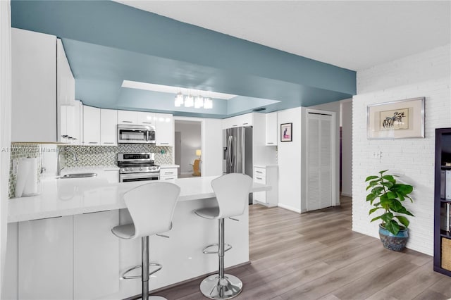 kitchen with tasteful backsplash, a breakfast bar, stainless steel appliances, light hardwood / wood-style flooring, and white cabinets