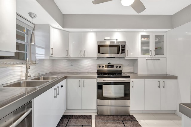 kitchen featuring stainless steel appliances, stainless steel countertops, white cabinets, backsplash, and glass insert cabinets