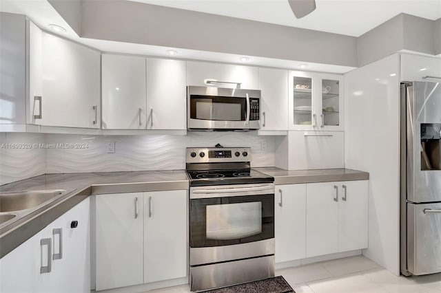 kitchen with decorative backsplash, appliances with stainless steel finishes, ceiling fan, light tile patterned floors, and white cabinets