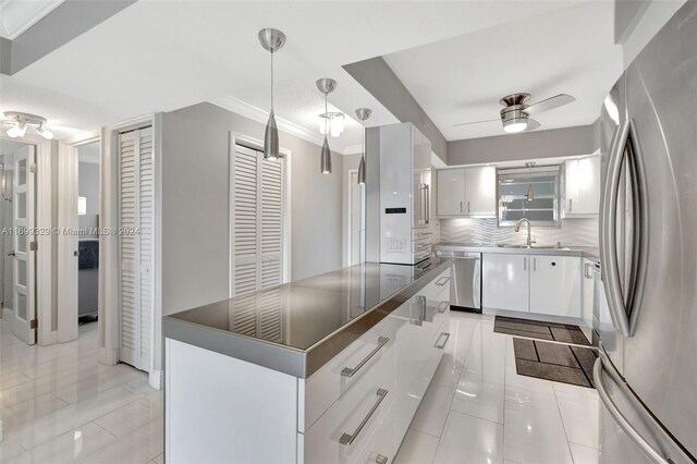 kitchen featuring backsplash, stainless steel appliances, light tile patterned floors, decorative light fixtures, and white cabinetry