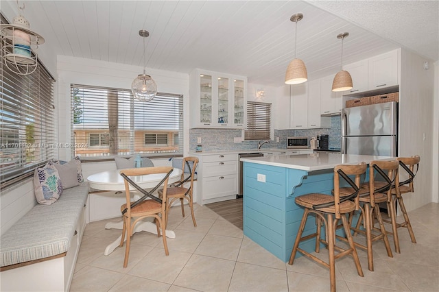 kitchen featuring white cabinetry, a center island, decorative light fixtures, decorative backsplash, and appliances with stainless steel finishes