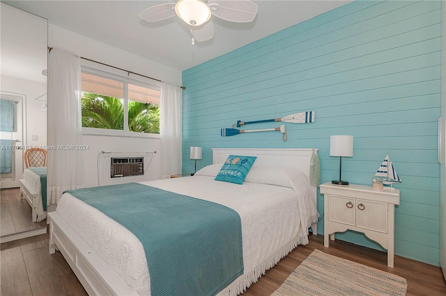 bedroom with hardwood / wood-style floors, wood walls, ceiling fan, a fireplace, and heating unit