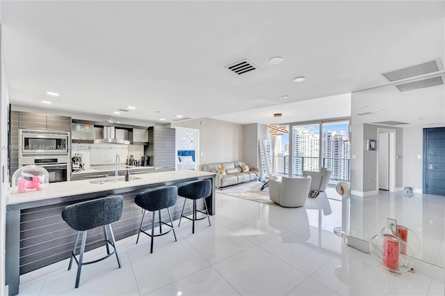 kitchen featuring a kitchen bar, appliances with stainless steel finishes, wall chimney exhaust hood, sink, and light tile patterned floors