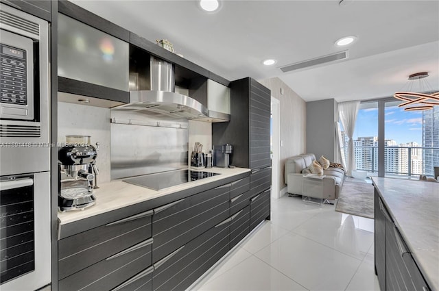 kitchen featuring black electric stovetop, white oven, light tile patterned floors, pendant lighting, and a notable chandelier