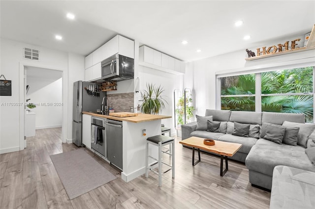 kitchen featuring white cabinetry, wood counters, light hardwood / wood-style floors, a breakfast bar, and appliances with stainless steel finishes