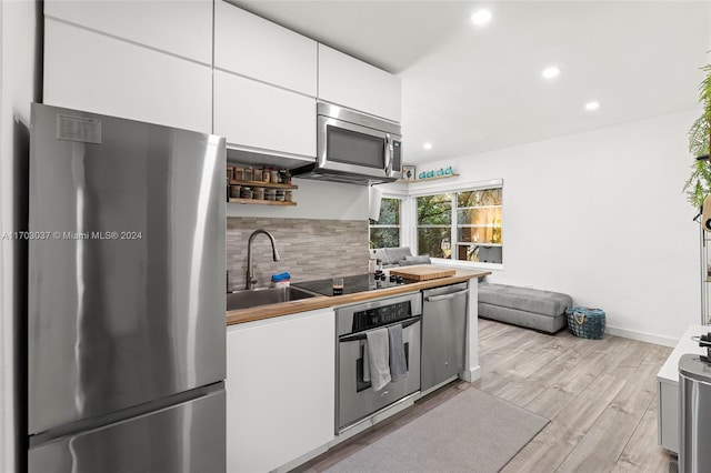 kitchen featuring white cabinetry, sink, tasteful backsplash, appliances with stainless steel finishes, and light wood-type flooring